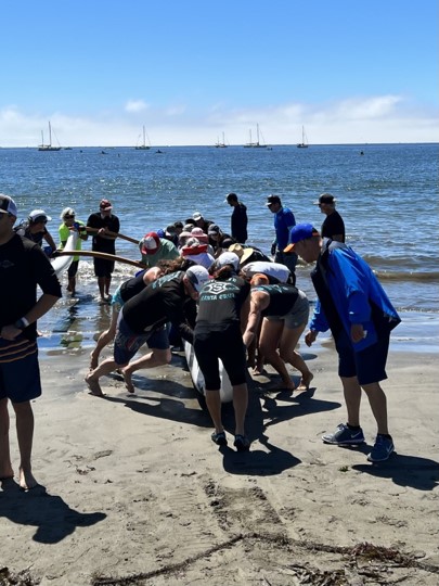 (Image description: A group of volunteers pushing an outrigger canoe into the ocean.)
